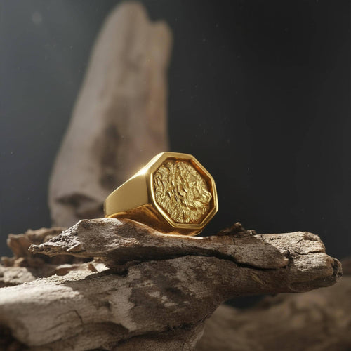 May include: A gold-colored ring with an octagonal face featuring a detailed relief design. The ring is set on a piece of weathered wood against a dark background. The ring's design is reminiscent of a coin.